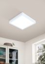 Quadratische LED-Deckenleuchte leuchtet hell in modernem, hellen Raum mit Fenster und Schrank im Hintergrund.