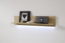Holzregal mit LED-Beleuchtung, Sanduhr, Kopfhörer, Lautsprecher und abstraktem Bild auf weißer Wand.