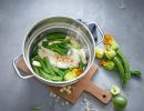Gedämpfter Fisch mit Zucchiniblüten, Lauch und Limette in Edelstahltopf auf Holzbrett, gesundes Rezept.