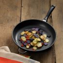 Bratkartoffeln mit lila und gelben Kartoffeln sowie roten Chilischoten in schwarzer Pfanne auf Holztisch.