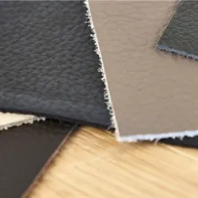 Nahaufnahme mehrerer Leder- oder Kunstledermuster in verschiedenen Farben wie Schwarz, Braun und Beige, ausgelegt auf einer Holzoberfläche – Symbol für Materialauswahl bei Möbeln.