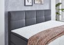 Modernes Boxspringbett mit grauem Kopfteil, weißer Matratze und rosa Decke vor grauer Wand im Schlafzimmer.