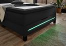 Modernes Boxspringbett in Dunkelgrau mit LED-Beleuchtung, Holzboden und Pflanzen im Schlafzimmer.