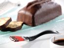 Schokoladenkuchen mit Schokoladenglasur, Pinsel mit Schokolade, Kuchenscheiben im Hintergrund, Nahaufnahme.