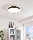 Moderne LED-Deckenleuchte rund, schwarz-weiß, leuchtet hell in hellem Wohnzimmer mit Regal und Pflanzen.