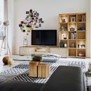 Modernes Wohnzimmer mit Holzmöbeln, Glas-Couchtisch, TV, Regal, Wandfotos und geometrischem Teppich.