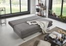 Graues Schlafsofa im modernen Wohnzimmer mit Decke, Couchtisch, Pflanzen und großem Fenster mit Gartenblick.