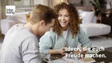 Lachendes Paar am Tisch mit Materialmustern und Einrichtungsplänen, daneben der Text „Ideen, die euch Freude machen“ und Interliving-Logo.