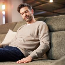 Mann sitzt entspannt auf grünem Sofa in Möbelausstellung und streicht mit der Hand über den Stoff.