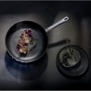 Moderne Bratpfanne mit gebratenem Fleisch, Kräutern und Gewürzen auf dunklem Untergrund, Food-Fotografie.