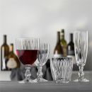 Vier elegante Kristallglu00e4ser mit Wein und Wasser auf Tisch, unscharfe Weinflaschen im Hintergrund, stilvolle Tischdeko.
