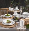Elegant gedeckter Esstisch mit weißem Porzellangeschirr, Glaskaraffe, Trauben, Brot und grünem Dekor.