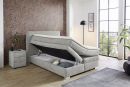 Modernes Boxspringbett mit Stauraumfunktion, grauem Stoffbezug, Nachttisch und großer Fensterfront im Schlafzimmer.