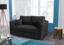Modernes, schwarzes Sofa mit Kissen im hellen Wohnzimmer vor großen Fenstern, Holztisch und blauer Akzentwand.