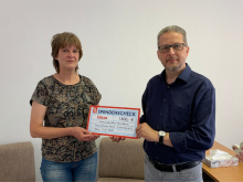Zwei Personen halten einen Spendenscheck über 1.500 Euro für einen gemeinnützigen Verein in einem Büro.