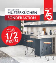 Moderne blaue Musterküche mit Kochinsel und Hockern; Jubiläumsaktion mit Hinweis auf Sonderpreise zum halben Preis in grossen Werbetafeln. Rabattdetails siehe Aktionsbedingungen.