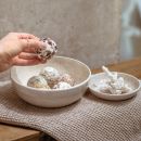 Hand nimmt vegane Energy Balls aus Keramikschale auf Holztisch, gesunde Snack-Alternative, Food-Fotografie.