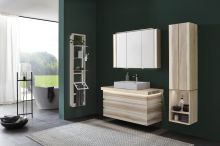 Modernes Badezimmer mit Holzwaschtisch, Spiegelschrank, Regalen und freistehender Badewanne vor grünem Akzent.