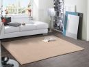 Modernes Wohnzimmer mit weißem Sofa, beigem Teppich, Buch, Lampe und Wandbildern auf dunklem Fliesenboden.