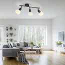 Moderne Wohnzimmer-Deckenleuchte mit drei Spots, helles Sofa, Holztisch, große Fenster, viele Zimmerpflanzen.