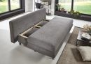 Graues Schlafsofa im modernen Wohnzimmer, ausgezogen als Bett, mit Pflanzen und großem Fenster im Hintergrund.