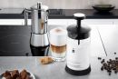 Edelstahl-Milchaufschäumer, Latte Macchiato, Kekse und Kaffeebohnen auf moderner Küchenarbeitsplatte.