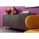 Modernes Sideboard mit Lochmuster vor lila Wand, dekoriert mit Obstschale, Glas und Vase, gelber Stuhl im Vordergrund.