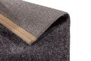 Nahaufnahme einer grauen Teppichkante mit rutschfester Unterseite und goldener Abschlussleiste, Teppichdetail.