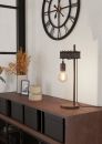Moderne Tischlampe mit Glühbirne auf Holzkommode, große Wanduhr, Dekoration und Pflanzen im Wohnzimmer.