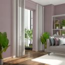 Modernes Wohnzimmer mit lila Wänden, grauem Sofa, Zimmerpflanzen, Vorhängen und viel Tageslicht.