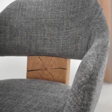 Detailaufnahme eines modernen Stuhls mit grauem Stoffbezug und sichtbarem Rückenverbindungselement aus massivem Holz mit natürlicher Rissstruktur.