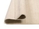 Beiger, gefalteter Teppich aus Naturfaser, Nahaufnahme, strukturierte Oberfläche, moderner Wohnstil.