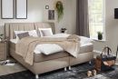 Modernes Boxspringbett mit gepolstertem Kopfteil, braunem Bezug und weißer Matratze auf Metallfüßen.