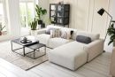 Modernes Wohnzimmer mit weißem Ecksofa, Couchtisch, Zimmerpflanzen und viel Tageslicht durch große Fenster.