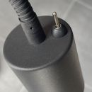 Nahaufnahme eines schwarzen Netzteils mit rundem Stecker und Kabel auf grauem Hintergrund, Ladegerät-Detail.