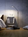 Moderne Stehlampe beleuchtet minimalistisches Schlafzimmer mit Betonwand, Bücherregal und Kissen auf Holzboden.