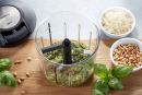 Frischer Basilikumpesto im Zerkleinerer, daneben geriebener Parmesan, Pinienkerne und frische Basilikumblätter.