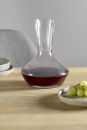 Karaffe mit Rotwein auf Holztisch, daneben grüne Weintrauben und Geschirr, modernes minimalistisches Design.