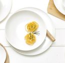 Tagliatelle-Nester mit frischem Rosmarin auf weißem Teller, minimalistisch angerichtet, italienische Pasta