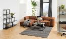 Modernes Wohnzimmer mit braunem Ecksofa, schwarzem Couchtisch, Regal, Teppich und großen Fenstern.