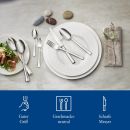 Edelstahl-Besteck auf weißem Teller mit Serviette, Steinen und Salat, modern gedeckter Tisch.