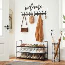 Flur mit Schuhregal, Garderobe, Jacke, Taschen, Hüten, Schlüsseln und „Welcome“-Schriftzug an der Wand.