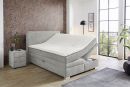 Modernes Boxspringbett mit verstellbarem Kopfteil in grauem Stoff, Schlafzimmer mit Holzfußboden und großer Fensterfront.