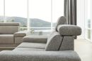 Modernes graues Sofa mit verstellbarer Kopfstütze vor großen Fenstern und Ausblick auf grüne Hügel und See.