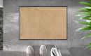 Beige Fußmatte auf grauem Boden, daneben grüne Pflanze und weiße Sneaker, moderne Eingangsdekoration.