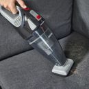 Handstaubsauger entfernt Tierhaare von grauem Sofa, Reinigung von Polstermöbeln, effektive Tierhaarentfernung.