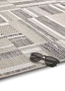 Moderner, rechteckiger Teppich in Beige-Grau mit geometrischem Muster und schwarzer Sonnenbrille am Rand.