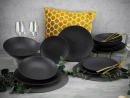 Schwarzes, modernes Tafelservice mit goldfarbenem Besteck, gelbem Kissen und Deko auf Holztisch.