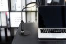 Moderne LED-Schreibtischlampe neben aufgeklapptem Laptop auf schwarzem Schreibtisch im Büro.