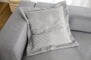Graues Sofakissen mit feiner Rillenstruktur auf hellgrauem Sofa, modernes Wohnzimmer, gemütliche Einrichtung.